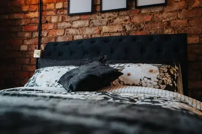 a black bed with pillows and a brick wall at Swiss Haven - Spacious 3 Bedroom House in Liverpool
