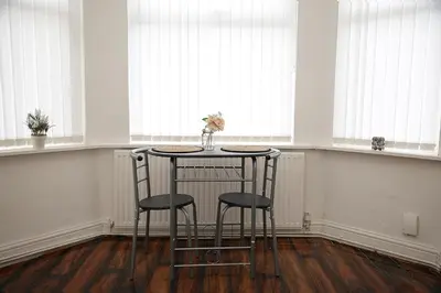 a table with two stools in a room with windows at Cosy Orrell Park Retreat Near Anfield and Aintree in Liverpool