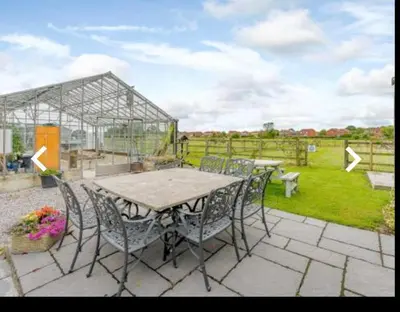 a table and chairs on a patio with a greenhouse at The Cow Shed in Longton