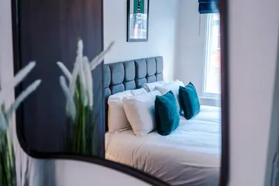 a bedroom with a bed with blue pillows and a mirror at Elysée Suites - Spacious 1 Bed Flat in Southport in Southport