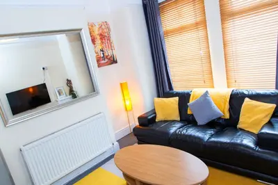 a living room with a black leather couch and a table at Newly Launched 3 Bedroom House with Free Parking in Litherland