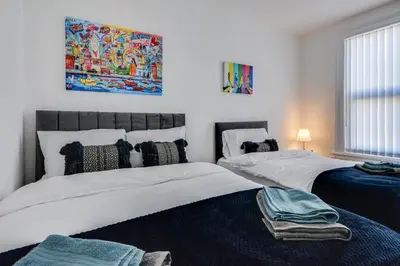 two beds in a bedroom with a painting on the wall at Stay With Alexandra 2 Free Parking - high speed Free Wifi close to stadiums in Liverpool