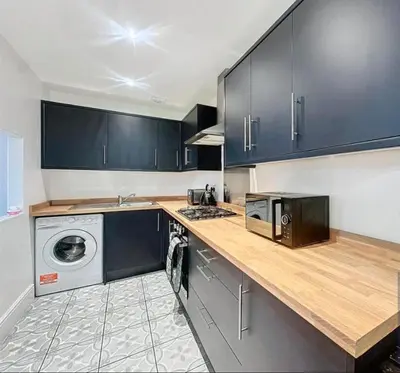 a kitchen with blue cabinets and a washer and dryer at Zetland House Apartment - First floor with garden and parking in Southport