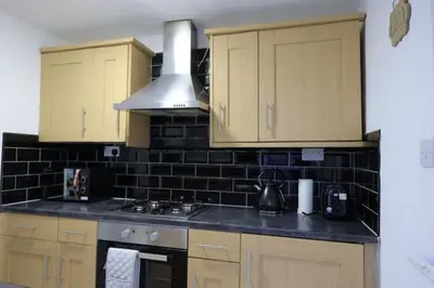 a kitchen with wooden cabinets and a black tiled wall at Providence Luxury Apartment in Liverpool
