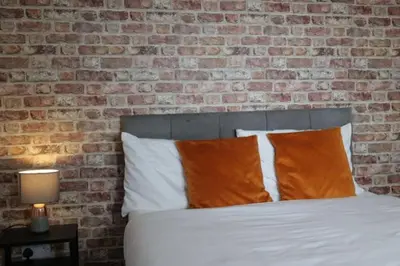 a bed with orange pillows in front of a brick wall at Providence Luxury Apartment in Liverpool