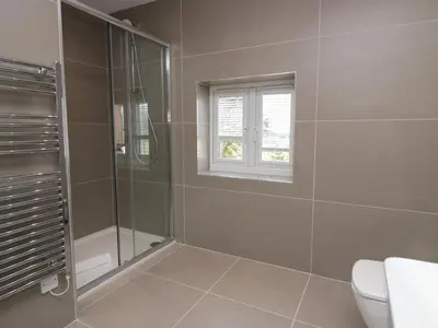 a bathroom with a shower and a toilet and a window at Edgemere Cottage in Grange Over Sands