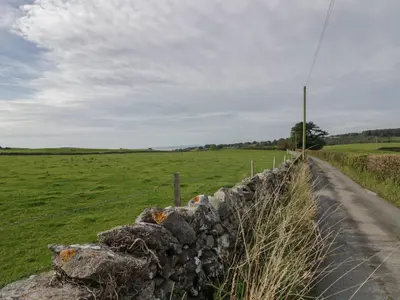 a stone fence on a road in a field at Edgemere Hideaway in Grange Over Sands