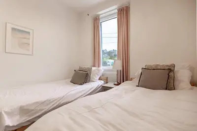 two beds in a white room with a window at SUN COTTAGE - Cosy Cottage in Ulverston with a log burner in Ulverston, Cumbria in Ulverston