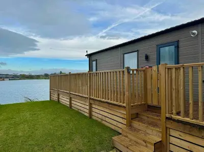a house with a wooden deck next to a body of water at Glenmoor Lodge in Clitheroe