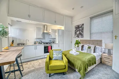 a bedroom with a green bed and a kitchen at Glendale House by Guestz in Lytham St Annes