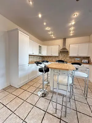 a kitchen with white cabinets and a table and stools at Abigail house in Westhoughton