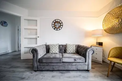 a living room with a couch and a clock on the wall at Spacious Apartment With A Terrace Style Rooftop in Cleveleys