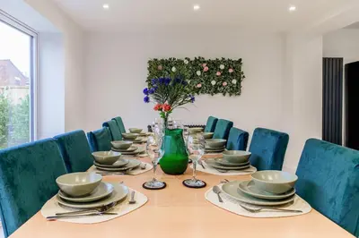 a dining room table with chairs and a green vase with flowers at Large 6-Bed house, Free Parking & Motorway Access in Ashton in Makerfield