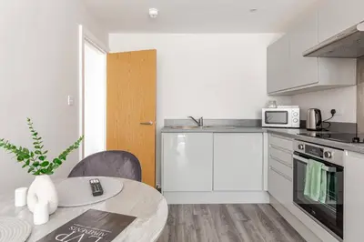 a white kitchen with a table and a microwave at 1-Bed Apartment With Sofa Bed in City Centre, Steps from Bold Street and Nightlife in Liverpool
