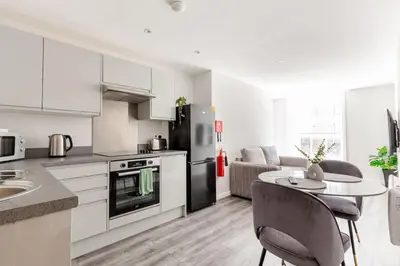 a kitchen with white cabinets and a table with chairs at 1-Bed Apartment With Sofa Bed in City Centre, Steps from Bold Street and Nightlife in Liverpool