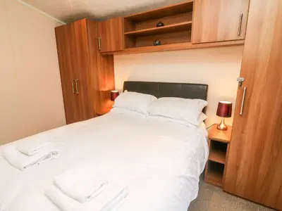 a bedroom with a large white bed with wooden cabinets at 6 Sherwood in Carnforth