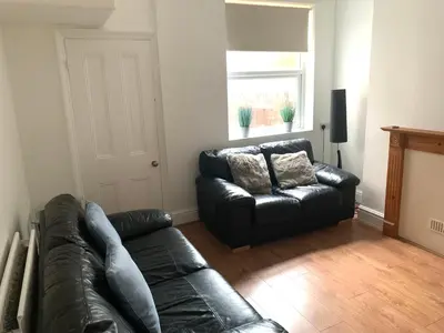 a living room with a black leather couch and a window at Ormskirk lets in Ormskirk