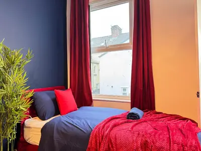 a bedroom with a bed and a window with red curtains at TV Every Bedroom 4 Bed 2 Bath Free Parking in Liverpool