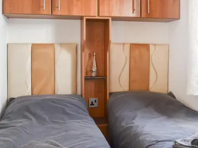 two beds in a bedroom with wooden cabinets at Cookies Corner in Millom