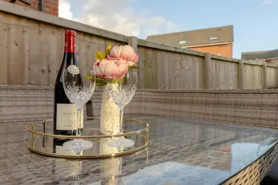 a glass table with a bottle of wine and flowers at Foxglove Haven- 3-Bed Detached - Garden - Drive in Longridge