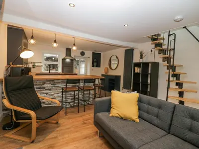 a living room with a gray couch and a kitchen at Cosy Logs Cottage in Grange Over Sands