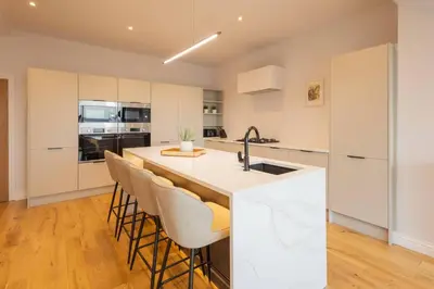 a kitchen with white cabinets and a kitchen island with bar stools at Host & Stay - Bay View House in Grange Over Sands