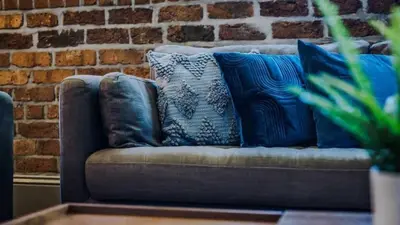 a couch with blue pillows in front of a brick wall at Central Warehouse Apt - Sleeps 8, Pet Friendly in Liverpool