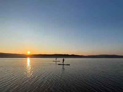 a man standing on a paddle board in a body of water at Beach Haven in Arnside