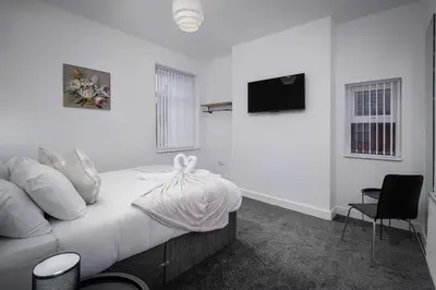 a bedroom with a bed with white sheets and a tv at Blackpool Abode - Shaw Heights in Blackpool