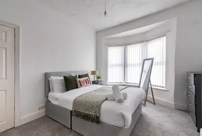 a bedroom with a large bed with white walls and windows at Spacious 4-Bedroom Home Close to Liverpool City Centre in Liverpool