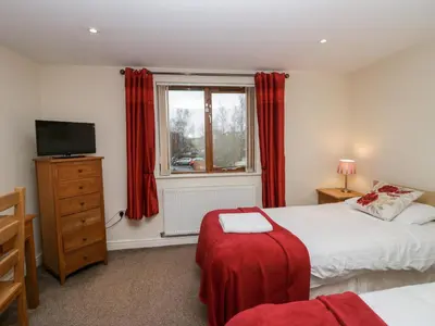 a bedroom with two beds and a window with red curtains at 4 Teal House in Carnforth