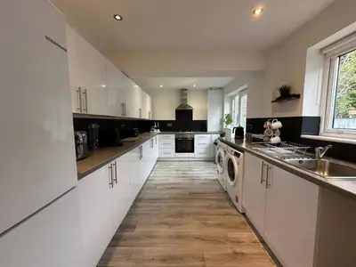 a large kitchen with white cabinets and a washer and dryer at Spacious 5 bedroom house in Fazakerley