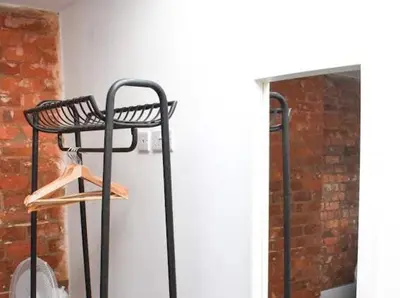 a black iron rack with a wooden hanger next to a brick wall at Castle Street 2 Bedroomed Next to The IVY in Liverpool