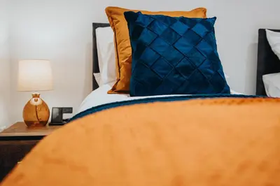 a bed with a blue and orange pillow and a nightstand at Brighton Street Apartment - 2 Bedroom Free Wi-Fi and Parking in Wallasey
