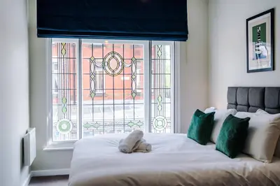 a bed with a teddy bear on it in front of a window at Elysée Suites - Stylish 1 Bed Flat in Southport in Southport