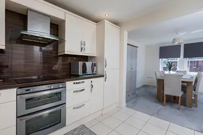 a kitchen with white cabinets and a dining room with a table at Spacious Luxurious Serviced Accommodation 6 in Barrow in Furness