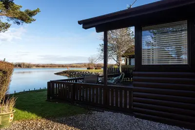 a house with a balcony and a lake at Sandmartin Lodge a lakeshore haven at Pine Lake Resort in Carnforth