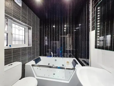 a black tiled bathroom with a tub and a toilet at house with hot tub in West Derby