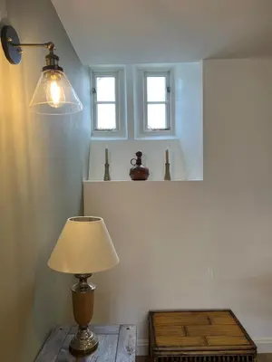 a lamp on a table in a room with two windows at Spacious & relaxing cottage stay with free parking in Cark