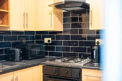a kitchen with a black tiled wall at Kirkdale Apartment in Liverpool