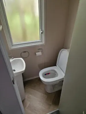 a bathroom with a toilet and a sink and a window at Lakeland Leaisure park Haven Caravan in Flookburgh