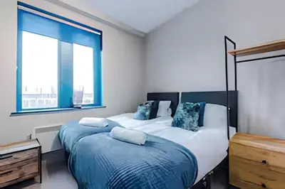 a bedroom with two beds and two windows at 1 Bedroom Apartment in Wigan Town Centre With Free Parking, by Short Term Digs Short Lets & Serviced Accommodation in Wigan