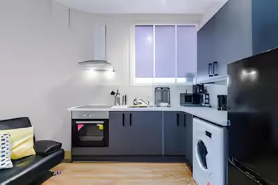a kitchen with white cabinets and a couch in a room at 1 Bedroom Apartment in Wigan Town Centre With Free Parking, by Short Term Digs Short Lets & Serviced Accommodation in Wigan