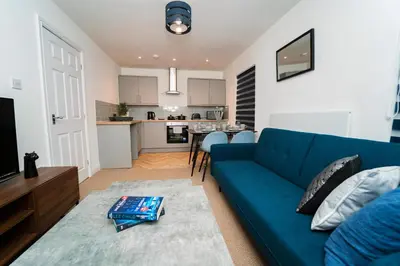 a living room with a blue couch and a kitchen at Stylish Self Check In Wigan Town Centre Apartment with Fast WiFi Ideal for Long Stays and Contractor Stays in Wigan