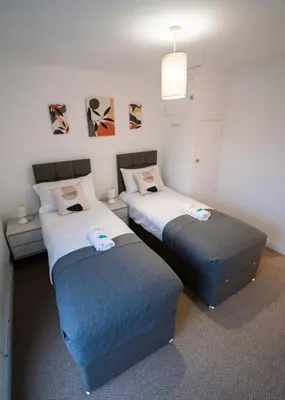 two beds in a room with two ottomans at Stylish Self Check In Wigan Town Centre Apartment with Fast WiFi Ideal for Long Stays and Contractor Stays in Wigan