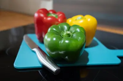 two peppers on a blue cutting board with a knife at Cozy Waterfront Apartment - Free Parking & Wi-Fi in Preston