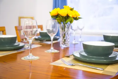 a wooden table with plates and glasses and yellow flowers at Lucky Home 7 - Ideal for Trade & Family - 2 Bedrooms - 2 Beds - Max 4 Guests - Close to BAE, Docks, Lake District, Beaches in Barrow in Furness