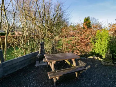 a wooden picnic table and bench in a garden at Elderflower Lodge in Grange Over Sands