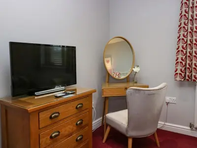 a television on a dresser with a chair and a mirror at 9 Swan House in Carnforth