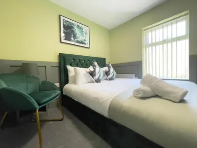 a bedroom with a large bed and a green chair at Serenity Holiday Apartments in Blackpool